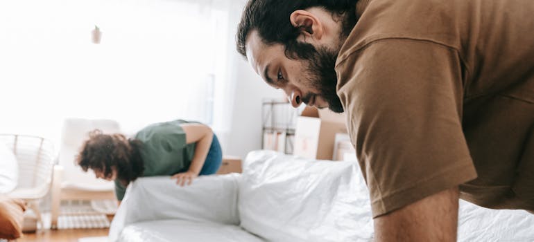 two people wrapping up a sofa to store it safely