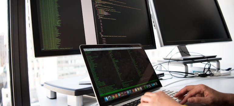 a man working on a laptop with four more monitors around him