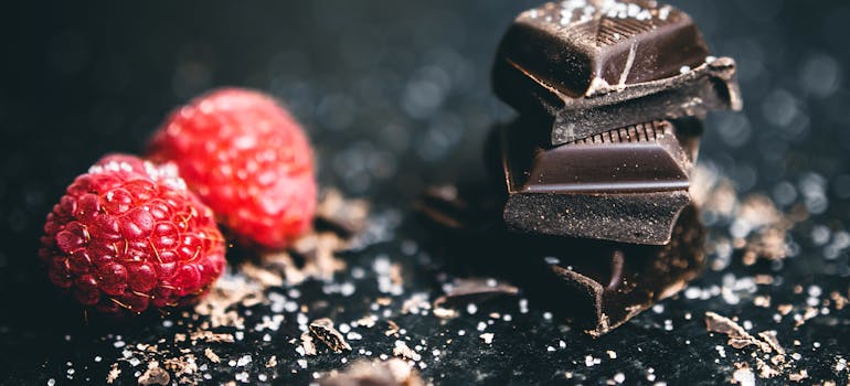 several pieces of dark chocolate, next to two raspberries