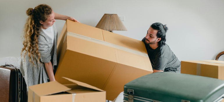 couple lifting a cardboard box and preparing for a move with the best movers clinton md has to offer