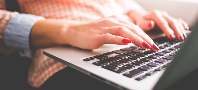 a woman with red nails, who wants to sell a house online is typing on her laptop