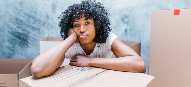 a woman leaning onto a cardboard box with a tired expression on her face