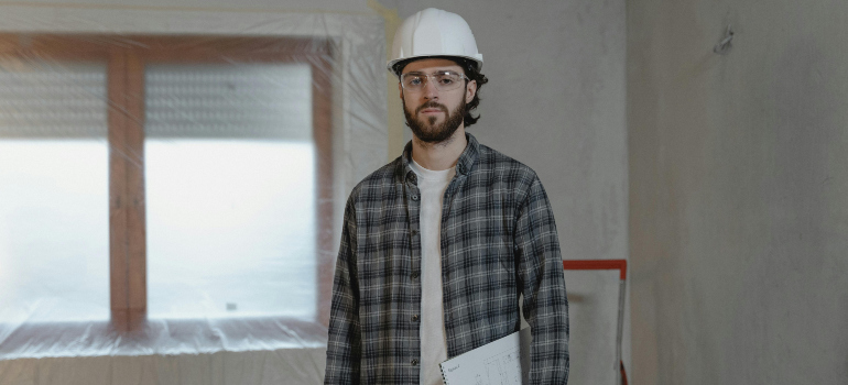 a man with a helmet is holding a clipboard in a house that is in the process of remodeling