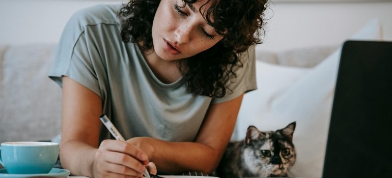 a girl writing something while her cat is beside her