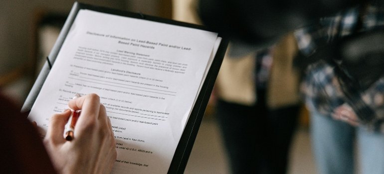 Person holding a clipboard and signing rental documents, preparing to complete the moving out of a rental process.