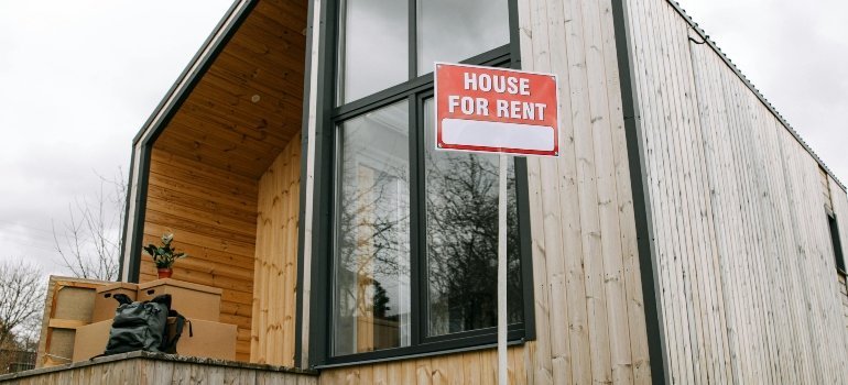 Exterior of a stylish wooden house with a red "House for Rent" sign in Falls Church, highlighting options for buying and renting in Falls Church.