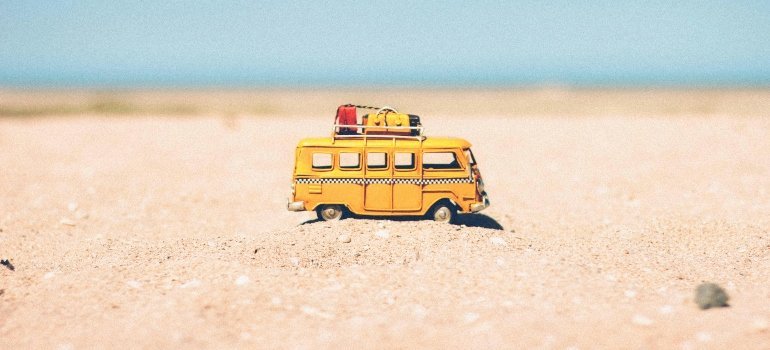A miniature yellow camper van sits on golden sand under the summer sun, symbolizing fun travel ahead.