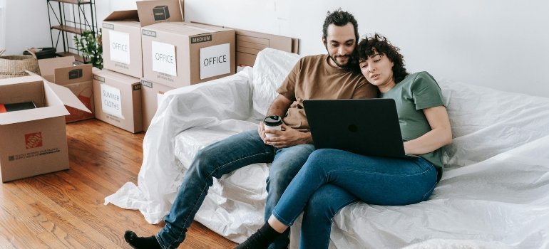 Couple sitting on couch surrounded by moving boxes, browsing for Maryland moving quote online.