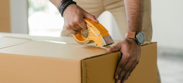 Close-up of a man using packing tape to seal a moving box to safely move large mirrors and other fragile items.