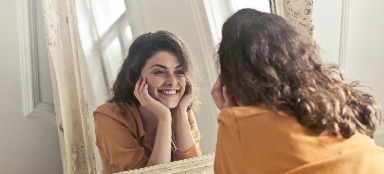 Woman looking happily at her reflection in a large mirror at home.