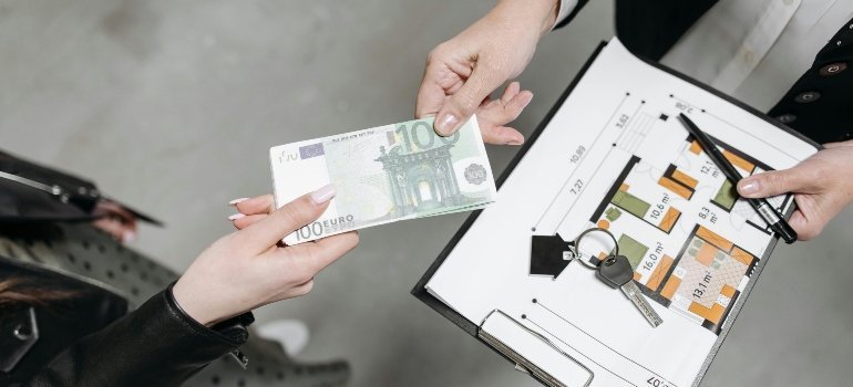 Person handing over cash while discussing property floor plan with keys in view.