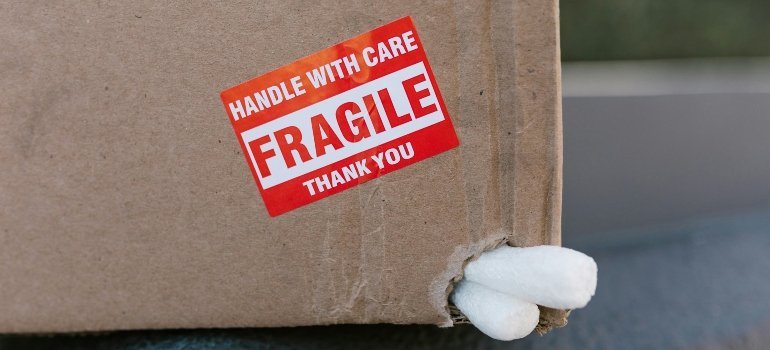 A cardboard box labeled "Fragile" with packing material sticking out from a torn corner.