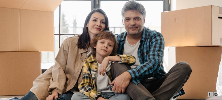 A family sitting close on the floor surrounded by moving boxes, showing the emotional side of moving for a job with a family.