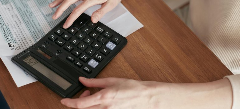 Close-up of a person calculating expenses on a wooden desk with a large calculator and financial documents.