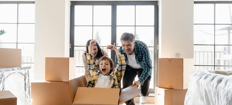 Parents and child laughing together while playing with moving boxes during relocation, representing the excitement of moving for a job with a family.