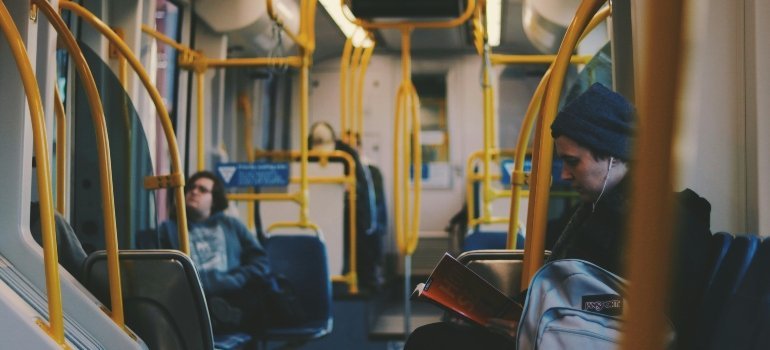 People seated inside a clean, modern public bus with yellow rails, some reading and relaxing.