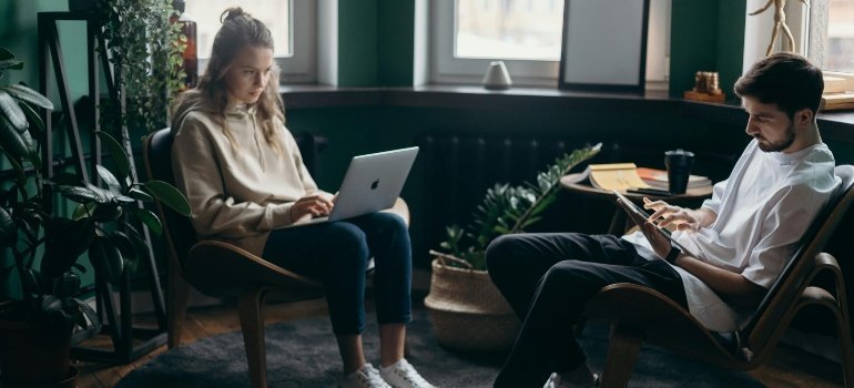 Two young professionals working comfortably from a stylish, cozy home office surrounded by plants.