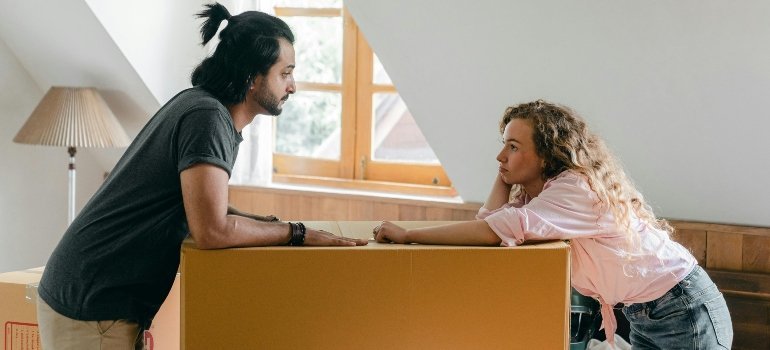 A couple leaning over a large box, deep in conversation while settling into their new space.