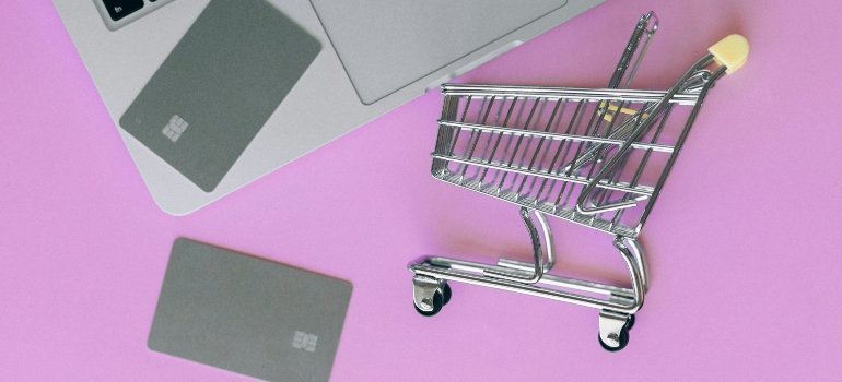 Mini shopping cart placed near laptop and credit cards, symbolizing online shopping and budget-friendly lifestyle.
