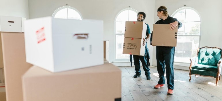 Two movers carrying cardboard boxes inside a bright, spacious home during a move-in.