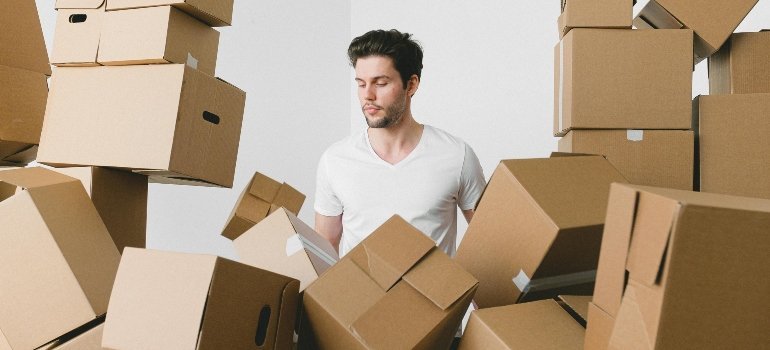 A man stands overwhelmed by a room filled with cardboard boxes during a moving process.