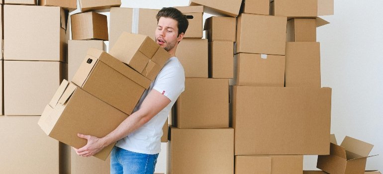 A man struggling to carry several cardboard boxes at once during a home move.