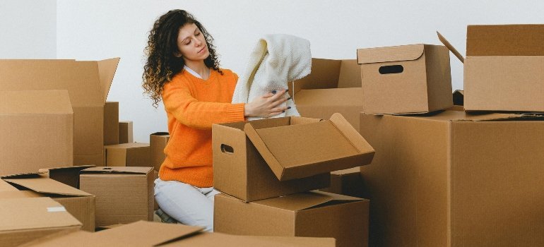A woman packing clothes into cardboard boxes — demonstrating “Moving Yourself And How to Handle It” with care and patience.