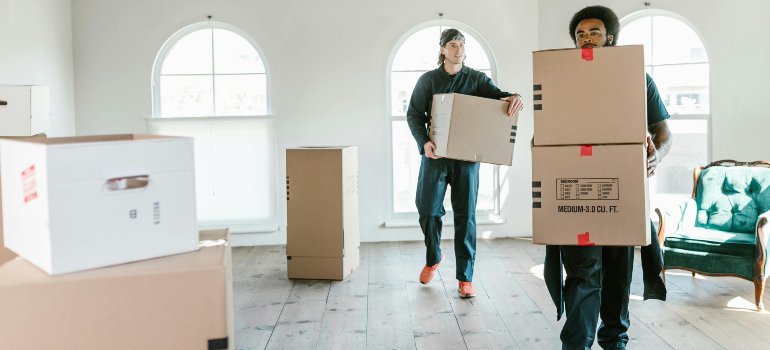 Two professional movers carry large cardboard boxes inside a bright office space during last-minute office moves in Bethesda.