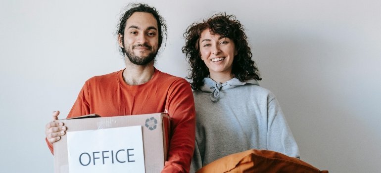Happy couple holding moving boxes and bags while preparing for Selling Everything and Leaving Town.