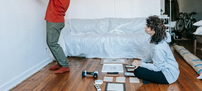 One person placing frames on the wall while another arranges them on the floor, hinting at Who Moves Out of Maryland with flair.