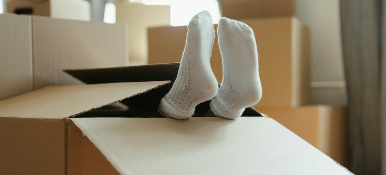 A pair of white-socked feet stick out of a big cardboard box—Support Your Teen Through a Move by keeping things playful.