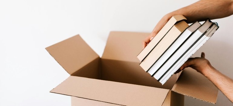 Hands carefully placing books into a cardboard box during a move.