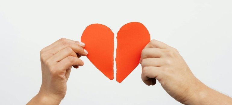Hands holding two halves of a torn red heart, symbolizing Moving Out After a Long Relationship.