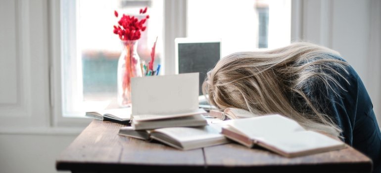 Exhausted woman resting her head on a desk full of notebooks after packing stress.