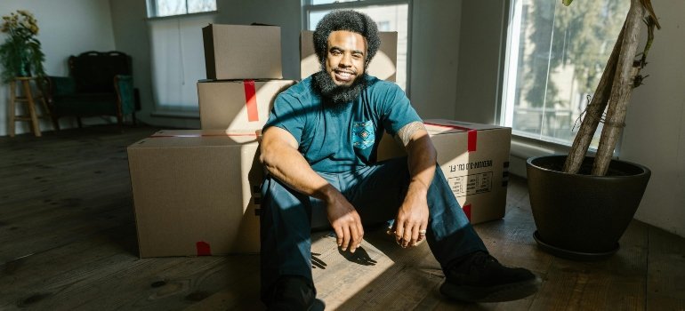 Man sitting on the floor, resting against packed boxes after a long day of moving.
