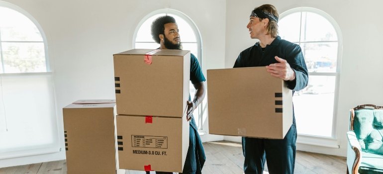 Two movers carrying boxes while talking during a house move.