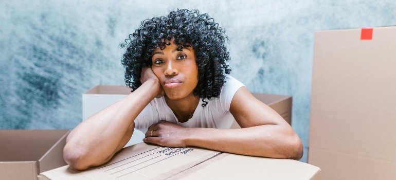 Woman leaning her head on a moving box with a thoughtful expression.