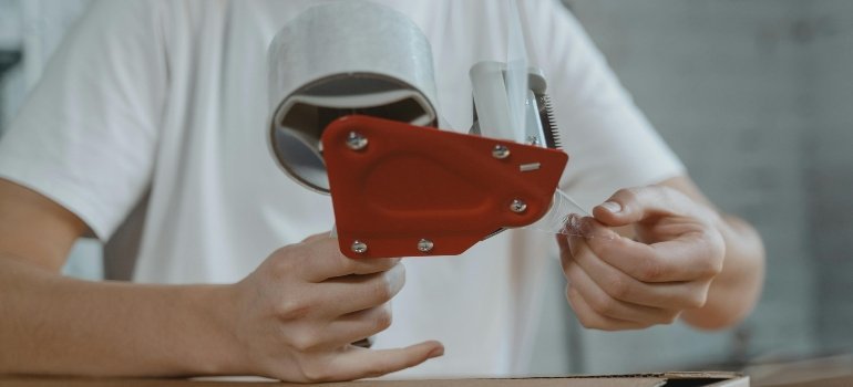 Close-up of hands using a tape dispenser to seal a moving box.