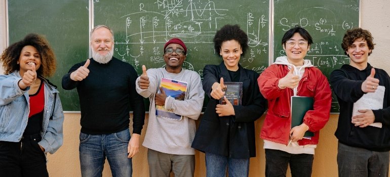 Teacher and students smile with thumbs up in front of a chalkboard—Support Your Teen Through a Move by meeting the school team.