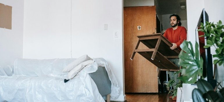 A man carefully carrying a wooden table through a narrow doorway while moving.