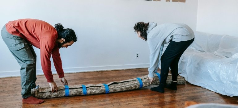 Two people rolling up a carpet together while preparing for a move.