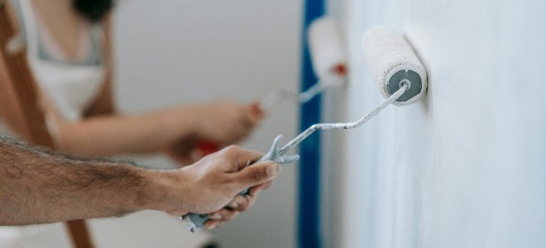 Close-up of hands rolling fresh white paint on a wall to prepare a rental unit for new tenants.