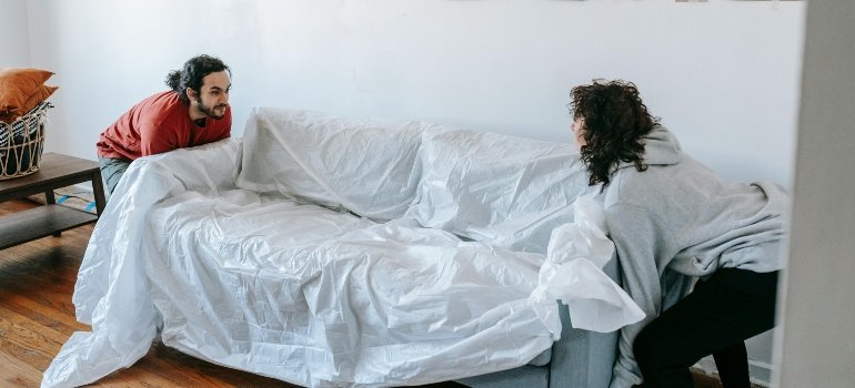 Two people lifting a covered couch during the moving process.