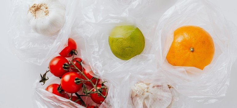 Fresh groceries including tomatoes, garlic, lime, and orange in plastic bags, symbolizing food costs.