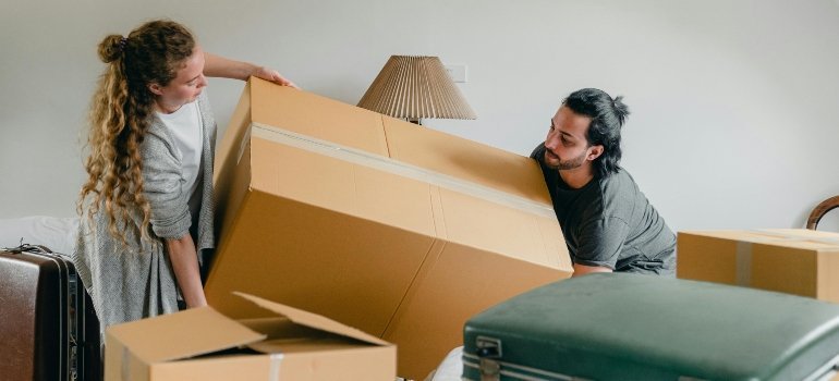 Two people lifting a large moving box while preparing to load it.