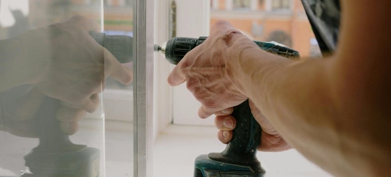 Person using a drill to adjust a window frame, part of the steps to Fix and Update Before Renting Your Alexandria Apartment.
