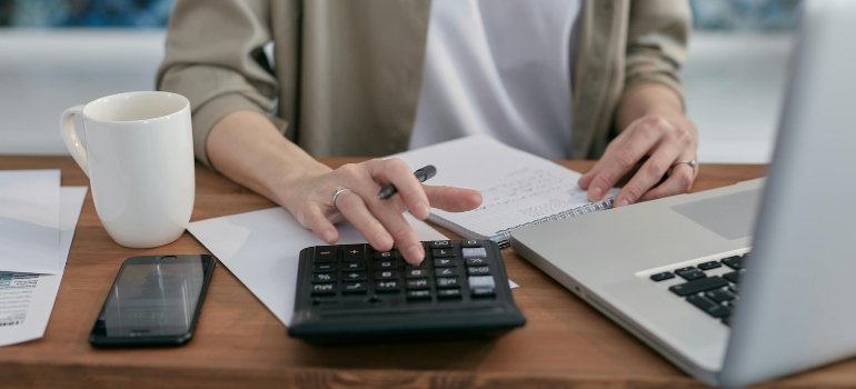 A person using a calculator and laptop while budgeting household expenses.