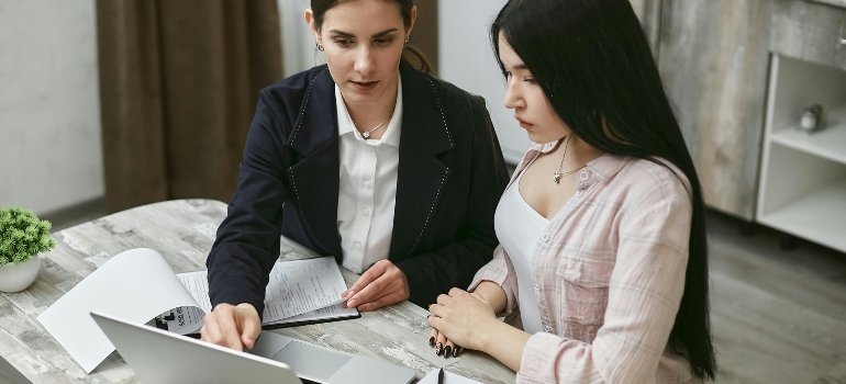 Women looking at a laptop together while researching choosing between hourly movers and flat-rate movers