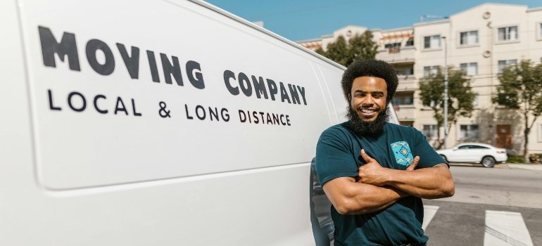 Mover in blue T-shirt and black pants standing beside white van, related to choosing between hourly movers and flat-rate movers