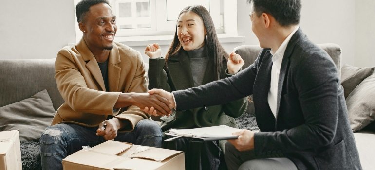 A smiling couple is sitting on a couch and discussing the best time to negotiate moving deals with their agent.